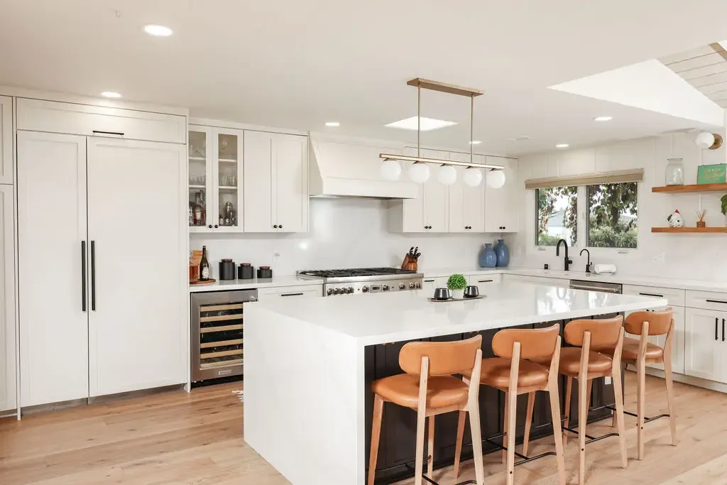 Bright modern kitchen with white shaker cabinets, waterfall island and leather counter stools